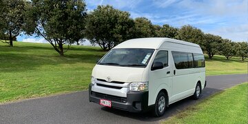 Front image of a white Toyota Hiace 12-seater minibus parked up with trees in the background