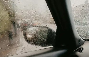 Rain-covered car window with blurred traffic outside