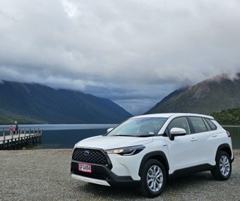 White SUV parked near a lake with mountains and a dock in the background