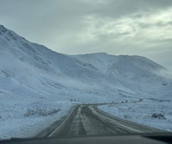 Snow-covered road winding through the mountains under a cloudy sky
