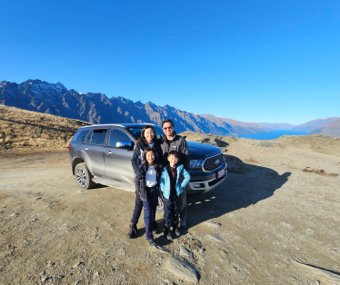 Family posing with an SUV on a scenic mountain road with a lake view